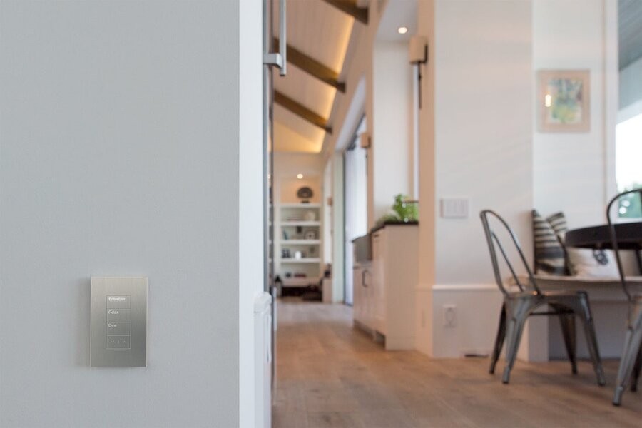 A living space illuminated by various lighting fixtures with a Lutron wall keypad in the forefront on a hallway wall.