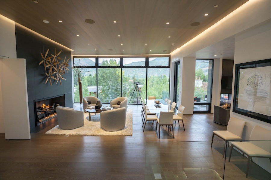 luxury living room with floor-to-ceiling windows overlooking a forest. In-ceiling speakers blend into the room’s design without detracting from the decor.