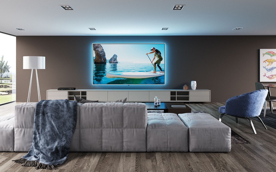 A media room with a comfortable couch, large screen with custom backlighting, and modern decor. 